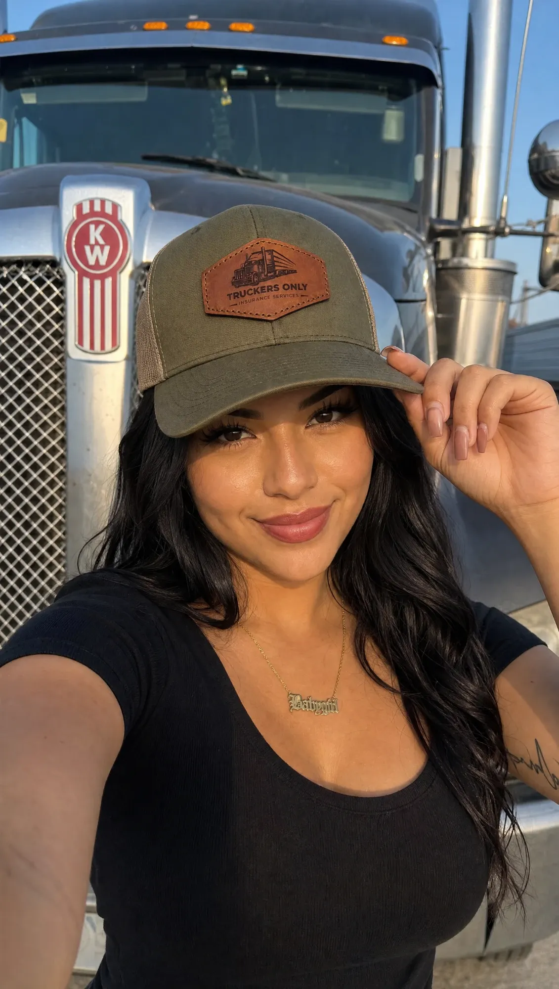 A driver in front of a Kenworth grille, tipping the brim of the 2026 Truckers Only cap
