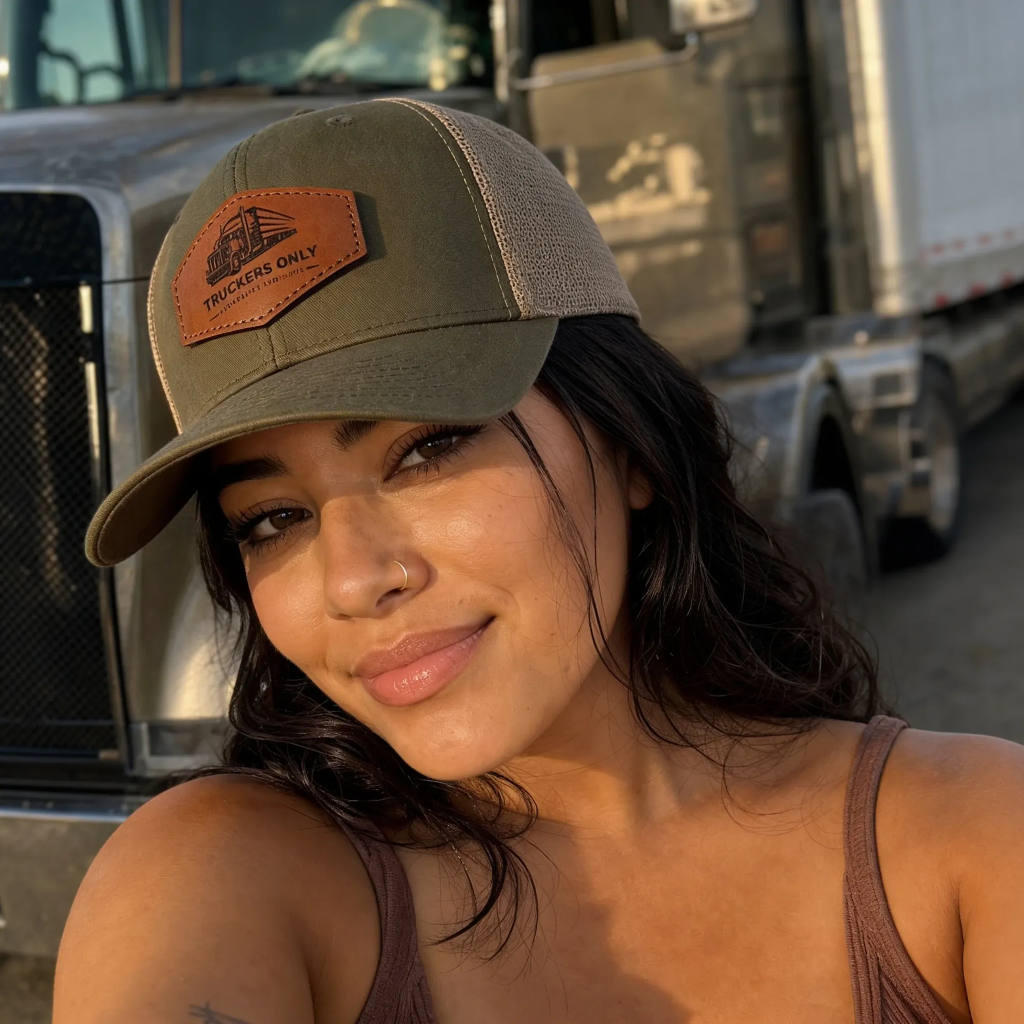 A driver in the 2026 Truckers Only cap at golden hour, her rig behind her